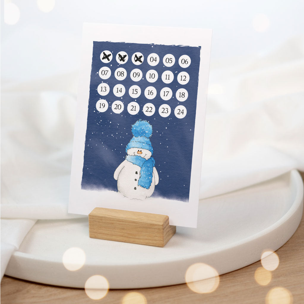 Adventskalender Karte mit Schneemann steht in Kartenhalter mit weihnachtlicher Deko