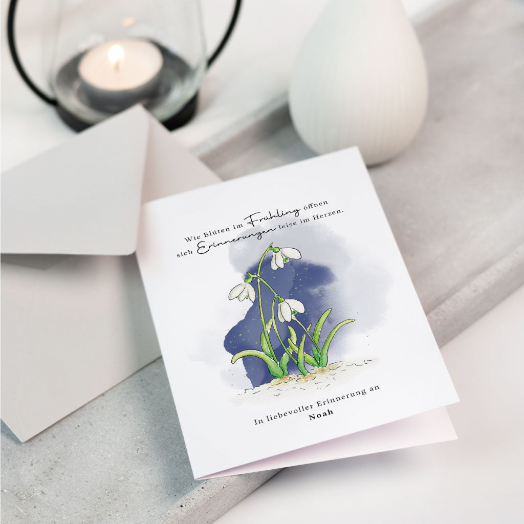 Personaliserbare Trauerkarte mit handgemaltem Schneeglöckchen Aquarellmotiv und einfühlsamem Trauerspruch, liebevoll arrangiert mit Umschlag, Kerze und Vase.