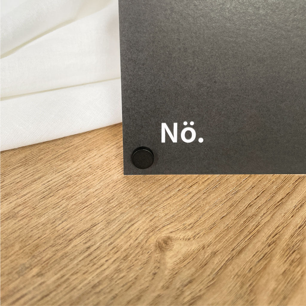 Nahaufnahme eines schwarzen Kartenständers mit „Nö.“: Pop Up Frame Kartenhalter, magnetisch schwarz als Fotohalter auf Holzoberfläche.