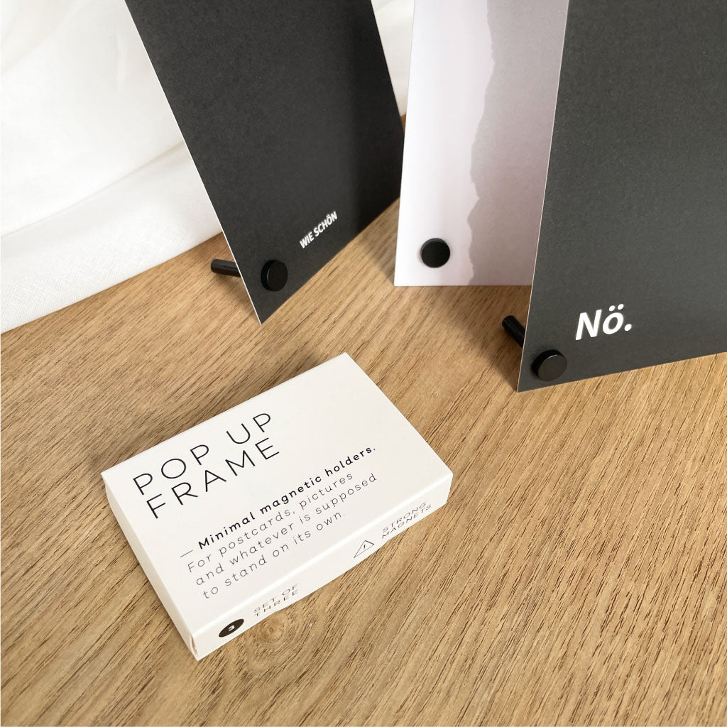 Verpackung der Kartenhalter in einer weißen Schachtel, im Hintergrund schwarz weiße Statement Postkarten