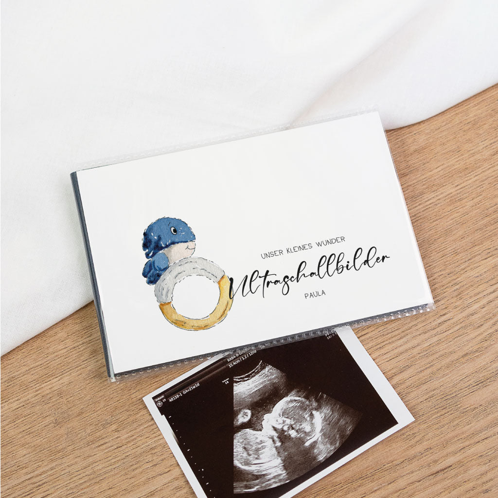 Schwarzes Einsteckalbum zur Ultraschallbilder Aufbewahrung, auf Holzoberfläche mit Ultraschallfoto – Covermotiv Wal und Schriftzug „Unser kleines Wunder“, personalisierbar mit Name