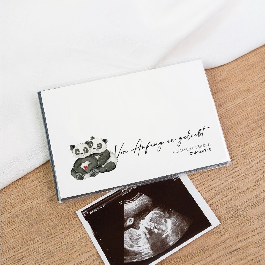 Ultraschallbilder Aufbewahrung: Einsteckalbum mit handgemalter Panda-Illustration und Schriftzug „Von Anfang an geliebt“, daneben Ultraschallfoto auf Holztisch.