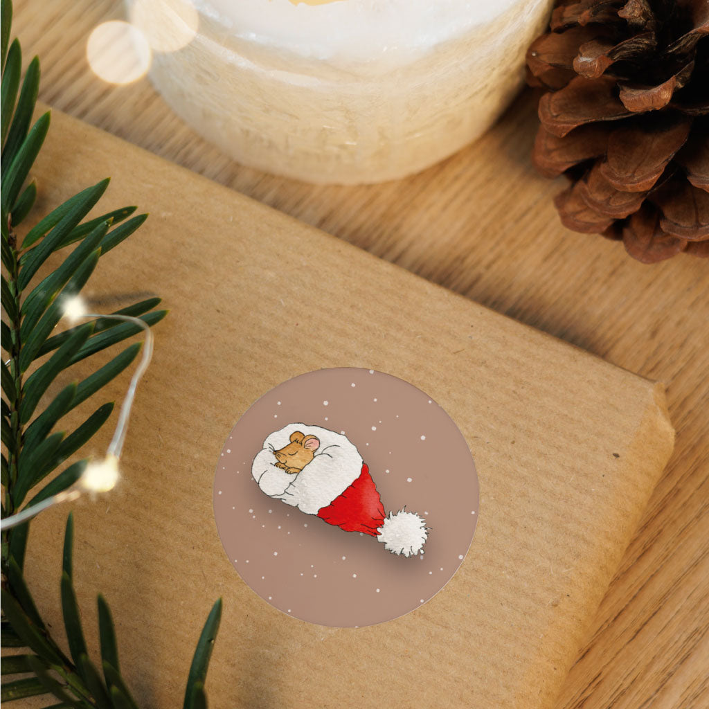 Runder Weihnachtssticker mit Aquarellmotiv einer Maus in Weihnachtsmütze auf Geschenkverpackung – stimmungsvolle Deko für Weihnachten.
