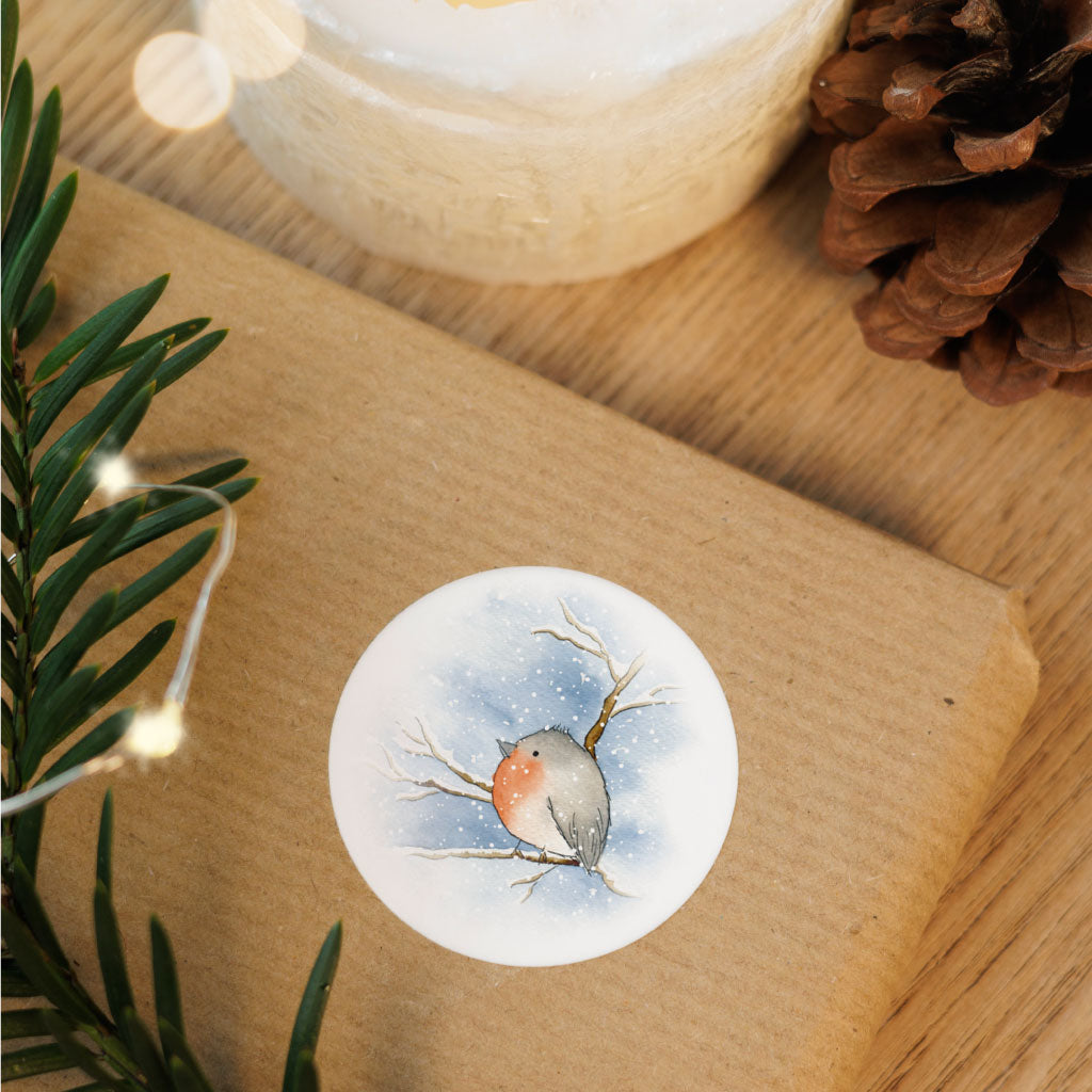 Runder Weihnachtsaufkleber mit Aquarell-Rotkehlchen auf braunem Geschenk – stimmungsvolle Dekoration für natürliche Geschenkverpackungen.