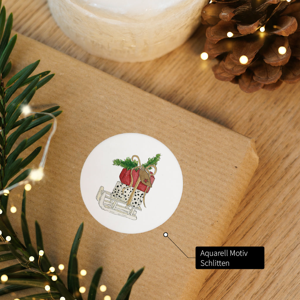 Sticker mit handgemaltem Schlitten Aquarell Motiv verziert ein liebevoll verpacktes Weihnachtsgeschenk.