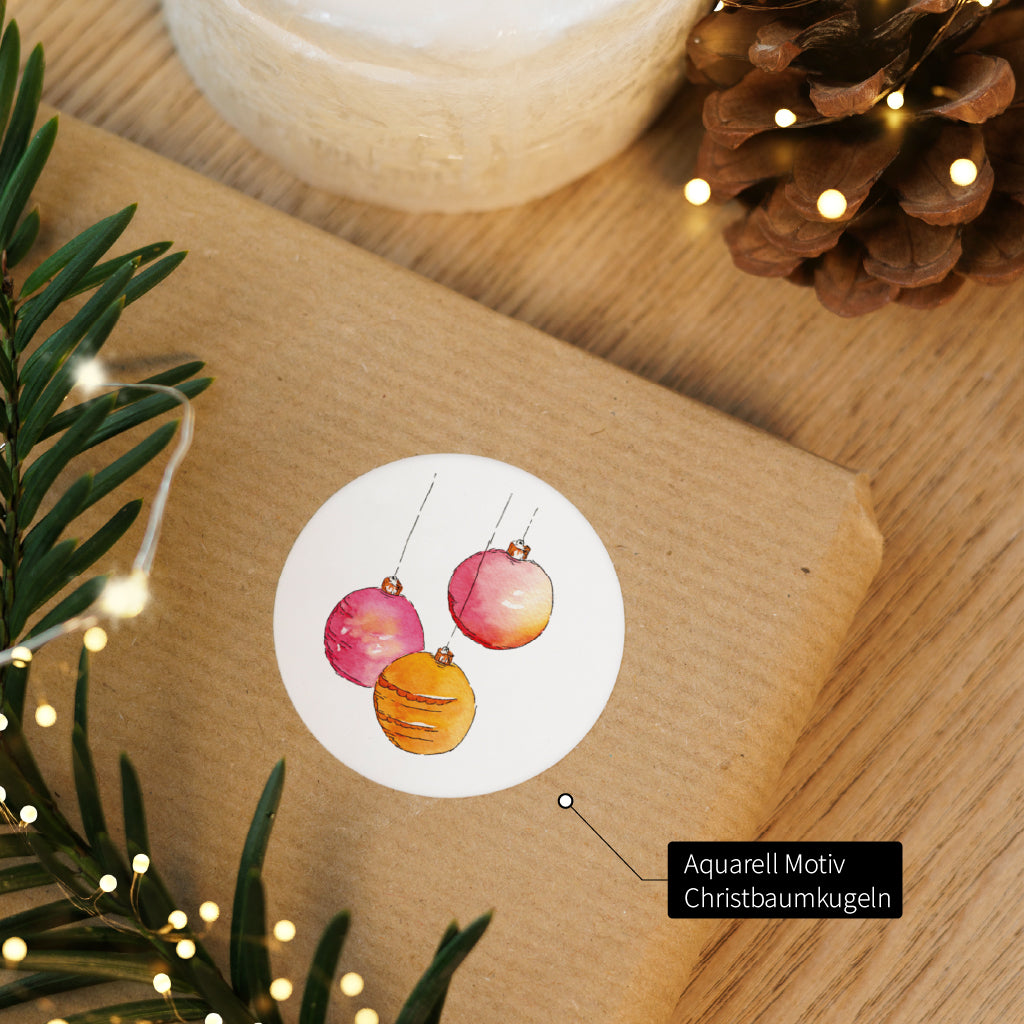 Runder Sticker mit Christbaumkugeln Aquarell Motiv klebt auf einem braunen Geschenkpaket im Advent.