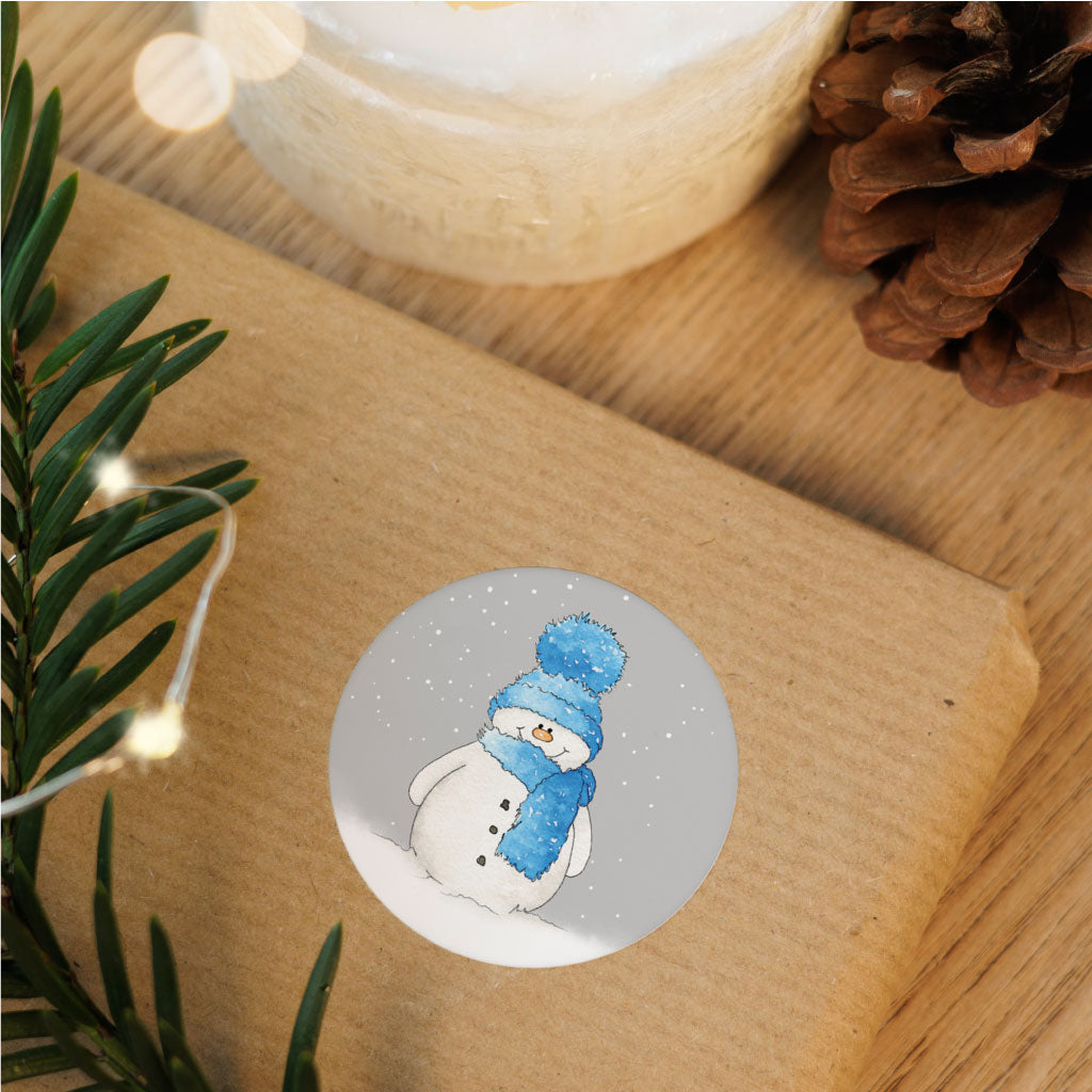 Runder Weihnachtsaufkleber mit Schneemannmotiv auf einem verpackten Geschenk – festliche Dekoration für die Adventszeit.