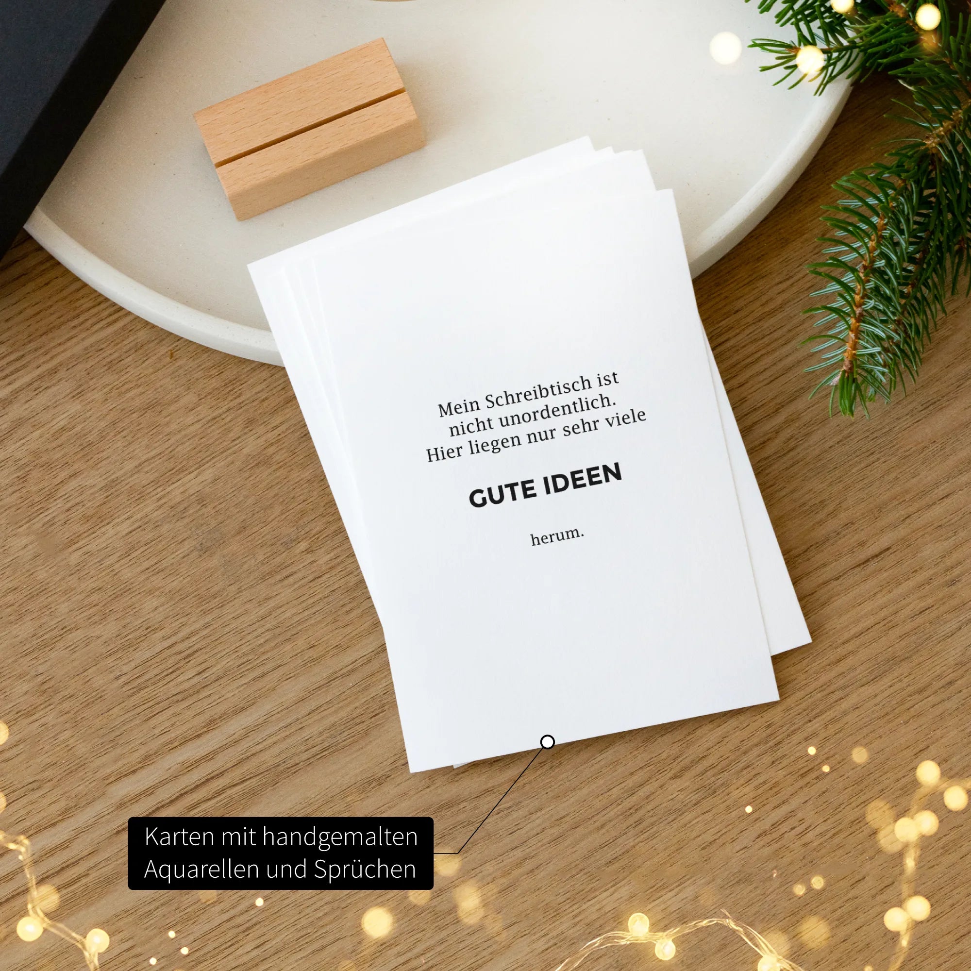 Karte mit humorvollem Spruch Gute Ideen aus dem Weihnachtsgeschenk-Set, Holz-Kartenhalter im Hintergrund, weihnachtliche Lichterkette