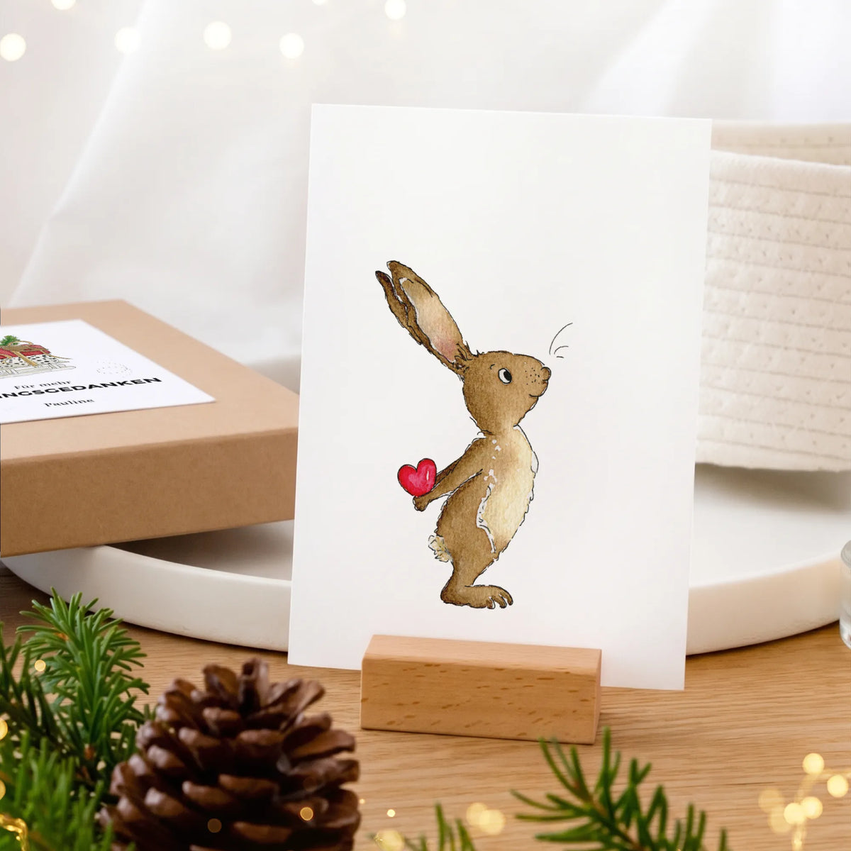 Aquarell Motiv Hase mit rotem Herz auf Karte im Holz-Kartenhalter, Geschenkbox im Hintergrund, Weihnachtsgeschenk Papeterie