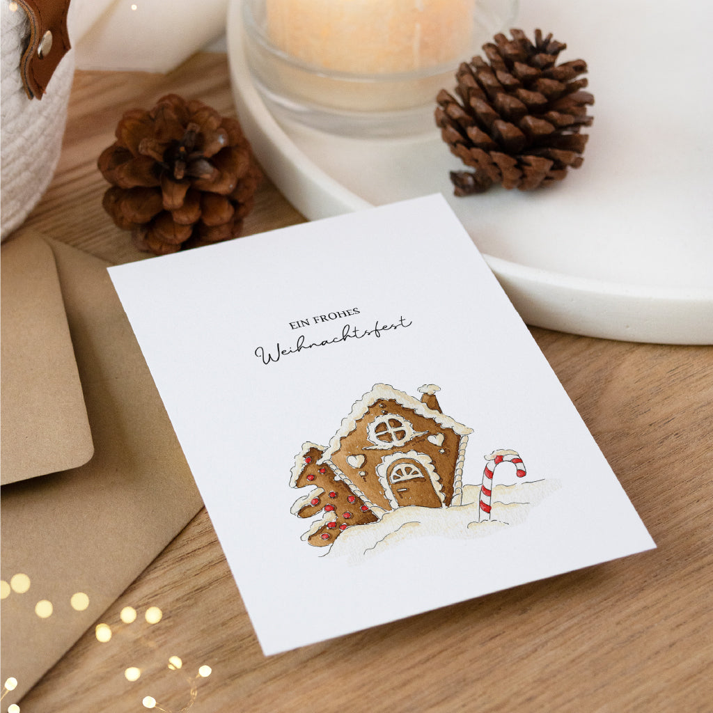 Schrägansicht der Weihnachtskarte mit Lebkuchenhaus Aquarell Motiv und braunem Umschlag.