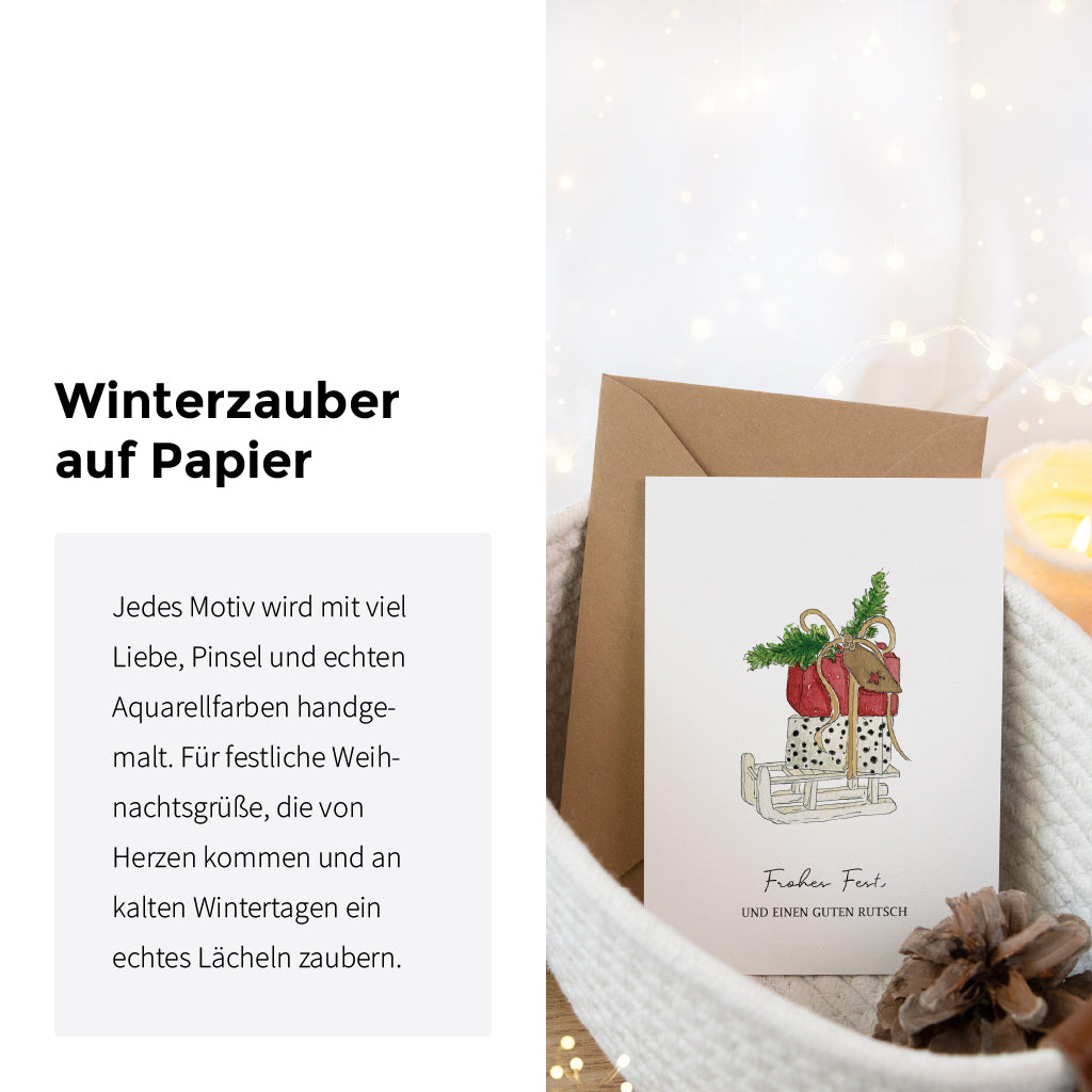 Textbild mit Aufschrift Winterzauber auf Papier neben einer Weihnachtskarte mit Schlitten Aquarell Motiv im Korb.