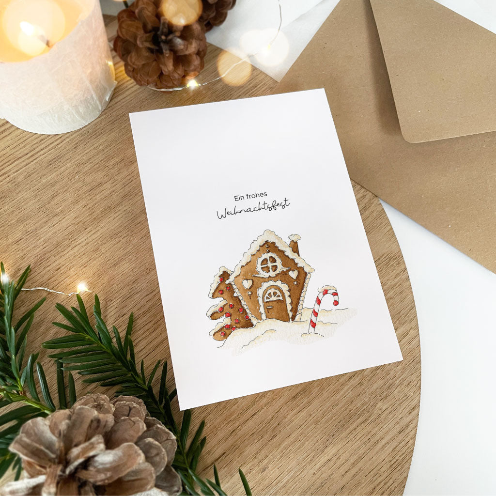 Karte liegt auf Kuvert, dahinter stimmungsvolle Weihnachtsdeko und Kerze