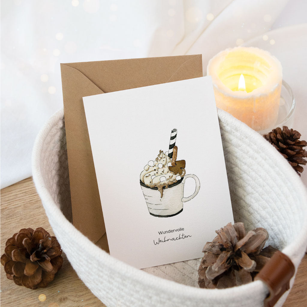 Weihnachtskarte mit Aquarellmotiv einer heißen Schokolade in einer Tasse und dem Spruch „Wundervolle Weihnachten“, stimmungsvoll dekoriert mit Kerze und Tannenzapfen.