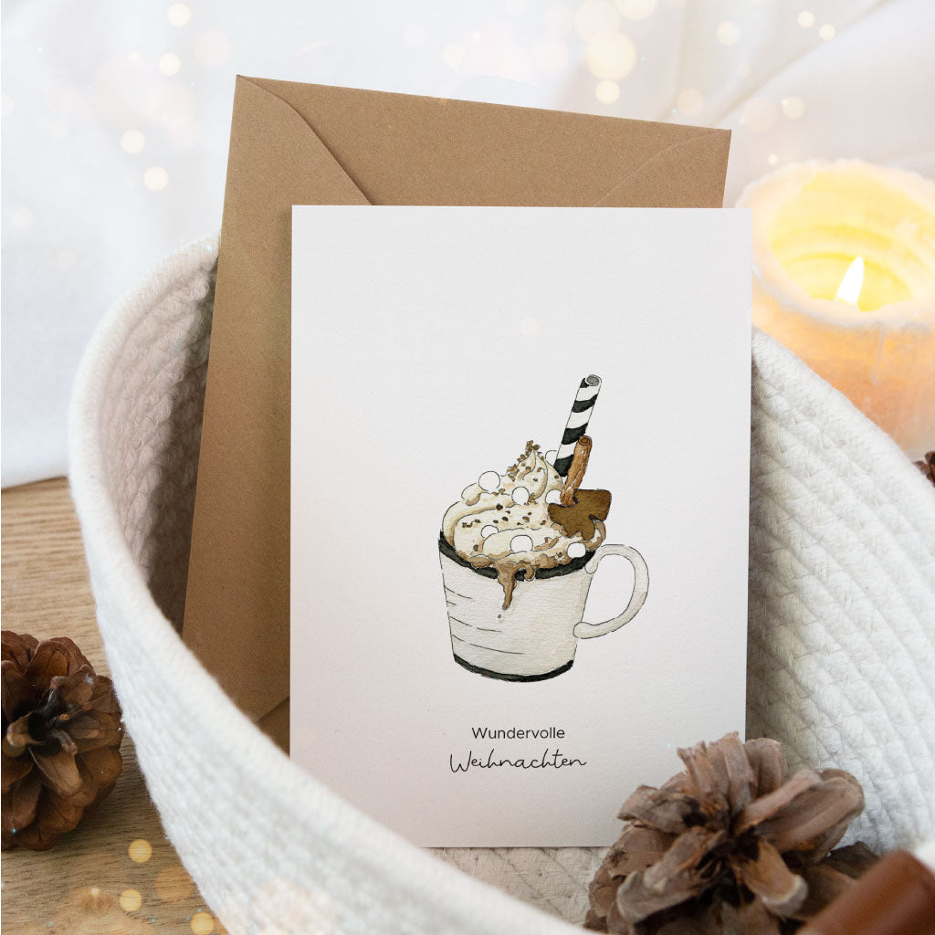 Postkarte mit handgemalter Tasse heißer Schokolade im Aquarellstil, liebevoll arrangiert mit Umschlag in einem weißen Korb – ideal zum Weihnachtsgeschenke verpacken.