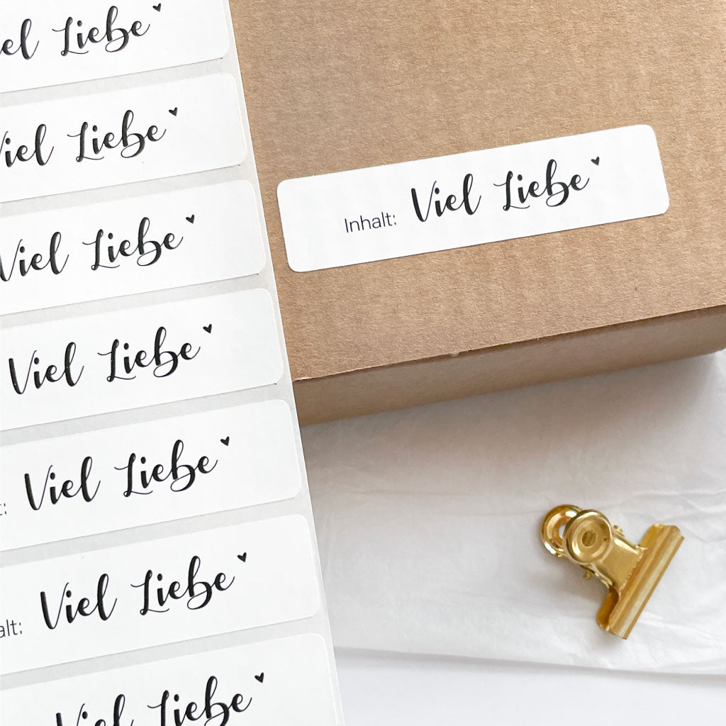Verpackungsaufkleber "Inhalt: Viel Liebe" klebt auf Karton, daneben Etiketten Rolle