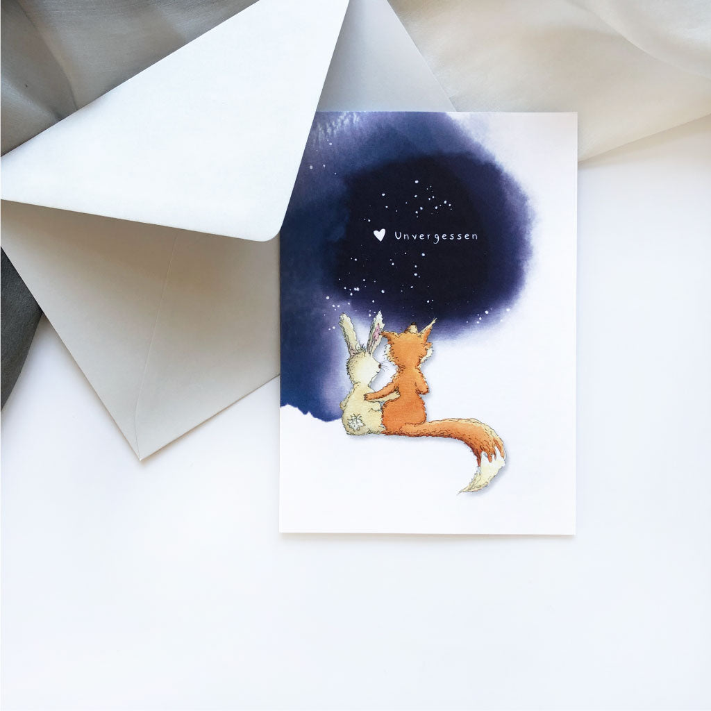Trauerkarte mit Text "Unvergessen" und Motiv mit Fuchs und Hase liegt in grauem Kuvert